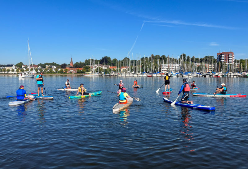 SUP Ausbildung - Teilnehmende auf ihren SUP Brettern auf dem Wasser und die Ausbilderin erklärt