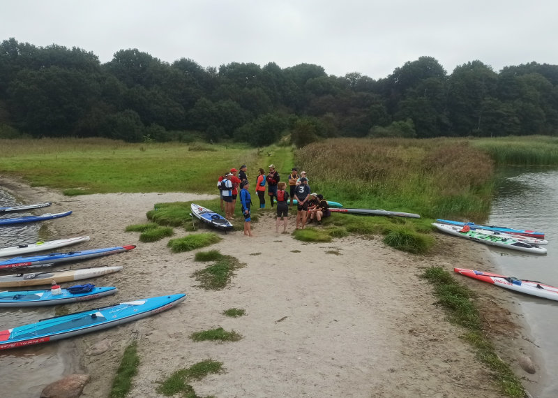 SUP Ausbildung: Pause der Teilnehmenden auf einer Landzunge. Die SUPs liegen am Strand.