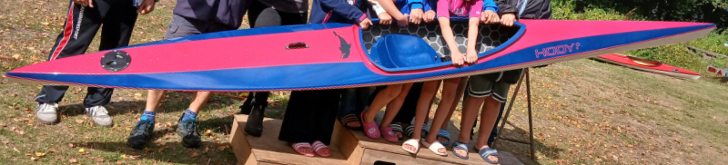 Viele Kinderhände halten das neue Kajak auf dem Podest 